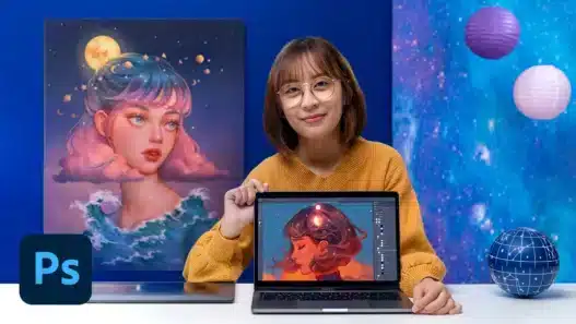 A woman in glasses and a yellow sweater sits at a desk, smiling and holding a laptop displaying digital art of a woman’s face. Behind her is a similar portrait painting. The Photoshop logo appears in the corner, hinting at creative courses online.