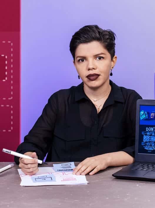 A person sits at a desk with papers, a pen, and a laptop displaying colorful design graphics. The background features icons, books, and WordPress symbols, suggesting a web or graphic design workspace for courses online.
