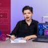A person sits at a desk with papers, a pen, and a laptop displaying colorful design graphics. The background features icons, books, and WordPress symbols, suggesting a web or graphic design workspace for courses online.