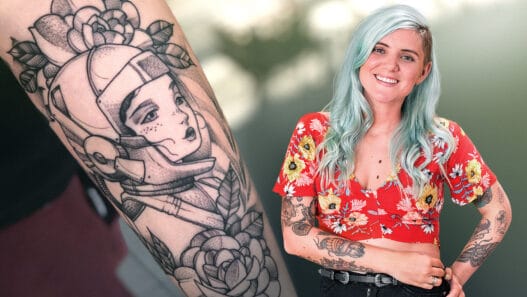 A smiling woman with light blue hair and tattoos, wearing a red floral top, stands next to a close-up of a black-and-white tattoo featuring a futuristic helmeted woman surrounded by flowers—perfect inspiration for courses online in tattoo artistry.