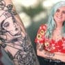 A smiling woman with light blue hair and tattoos, wearing a red floral top, stands next to a close-up of a black-and-white tattoo featuring a futuristic helmeted woman surrounded by flowers—perfect inspiration for courses online in tattoo artistry.