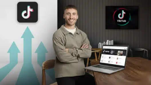 A smiling man sits at a desk with a laptop displaying TikTok on the screen. Behind him, a large TikTok logo and upward-pointing arrows are visible, suggesting growth or success on the platform.
