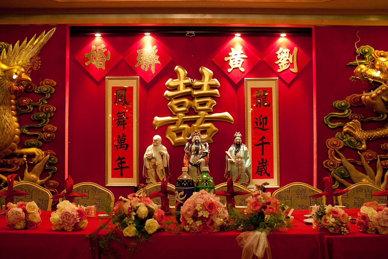 Decorated wedding reception venue with draped fabric, chandeliers, and arranged dining tables