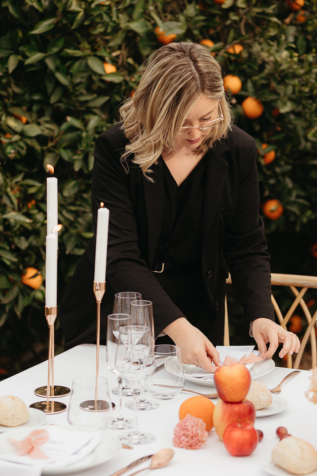 Professional wedding planner arranging candles and tableware at an outdoor event table setting