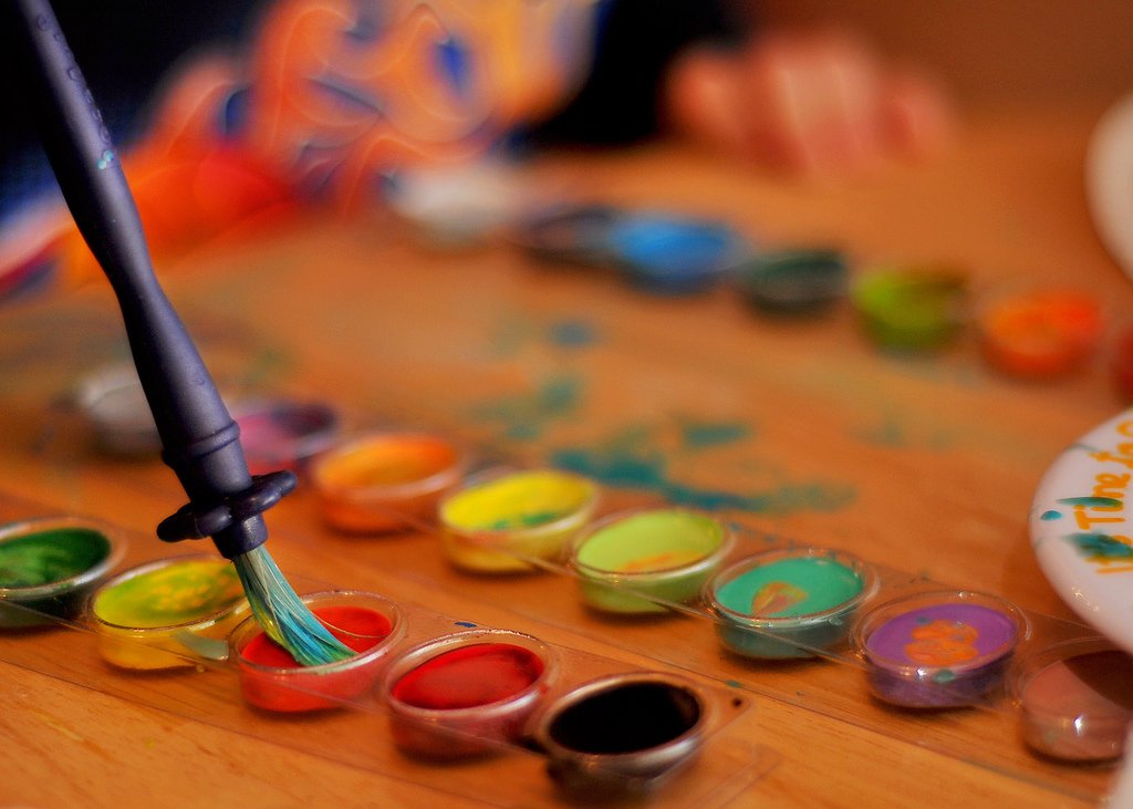 A paintbrush beside a set of watercolor pans