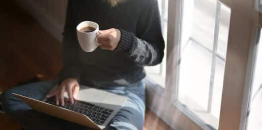 Woman studying on a laptop at home holding a coffee cup