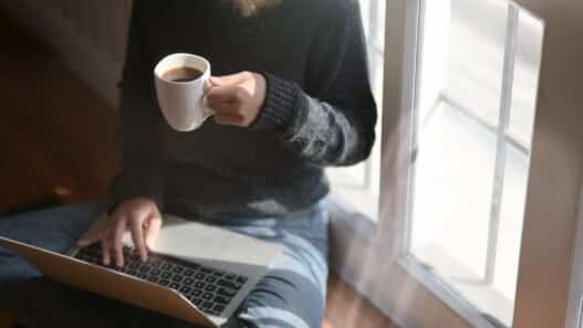 Woman studying on a laptop at home holding a coffee cup