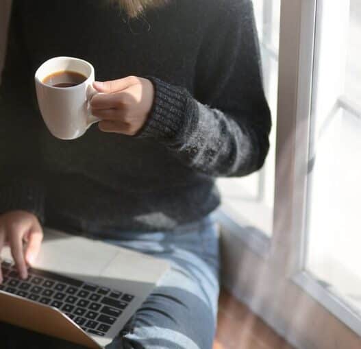 Woman studying on a laptop at home holding a coffee cup