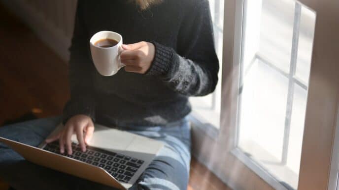 Woman studying on a laptop at home holding a coffee cup
