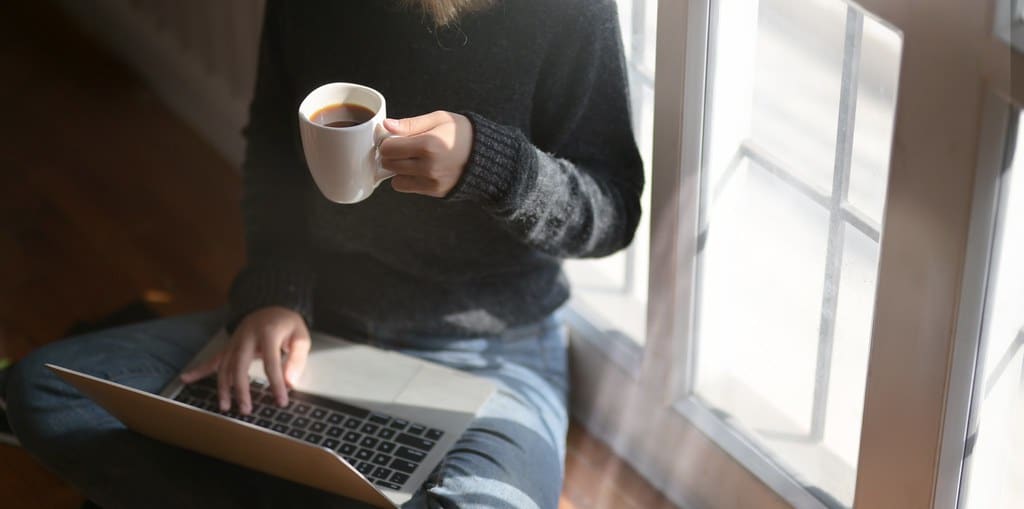 Woman studying on a laptop at home holding a coffee cup