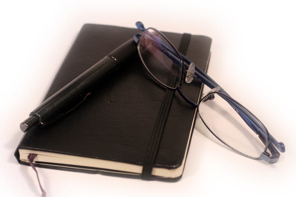 Black diary notebook with a pen and reading glasses
