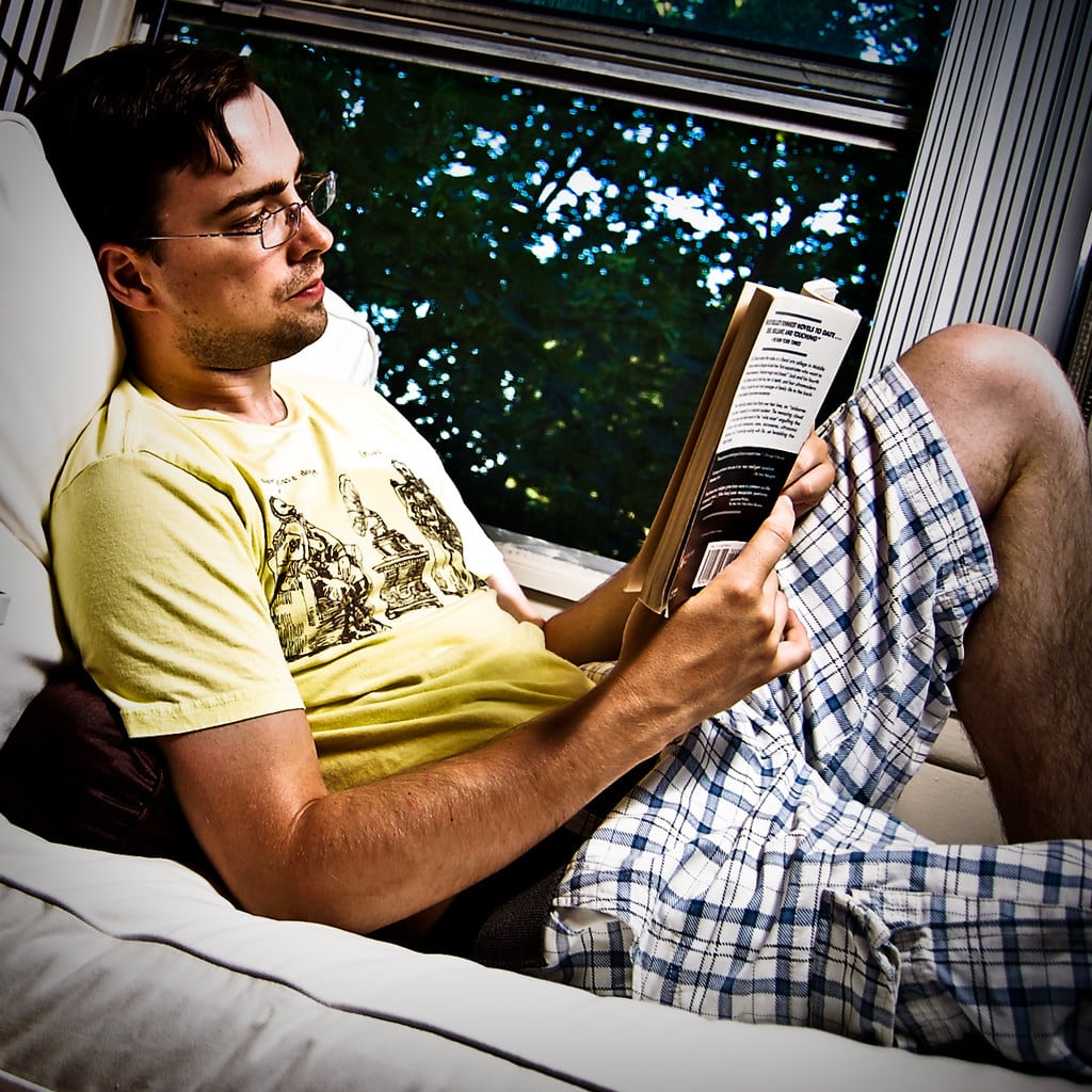 Young man reading a book on a couch by the window