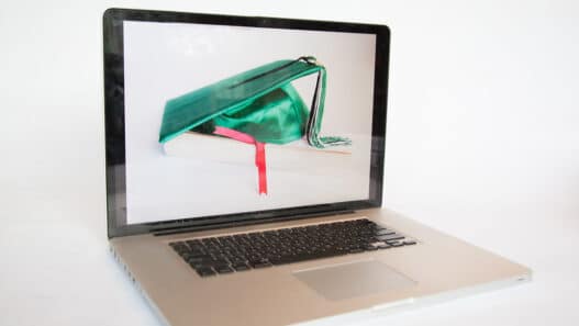 Laptop displaying a graduation cap resting on a book