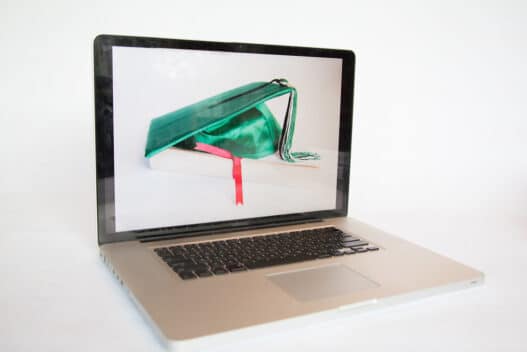 Laptop displaying a graduation cap resting on a book