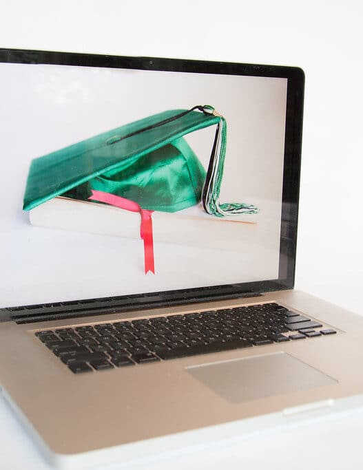 Laptop displaying a graduation cap resting on a book