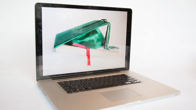 Laptop displaying a graduation cap resting on a book