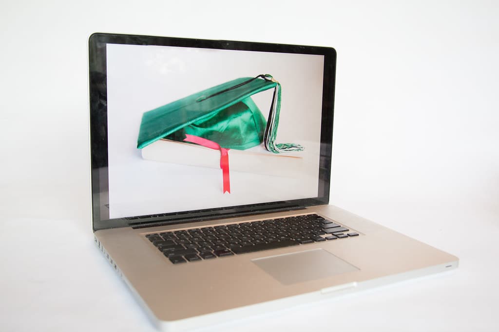 Laptop displaying a graduation cap resting on a book