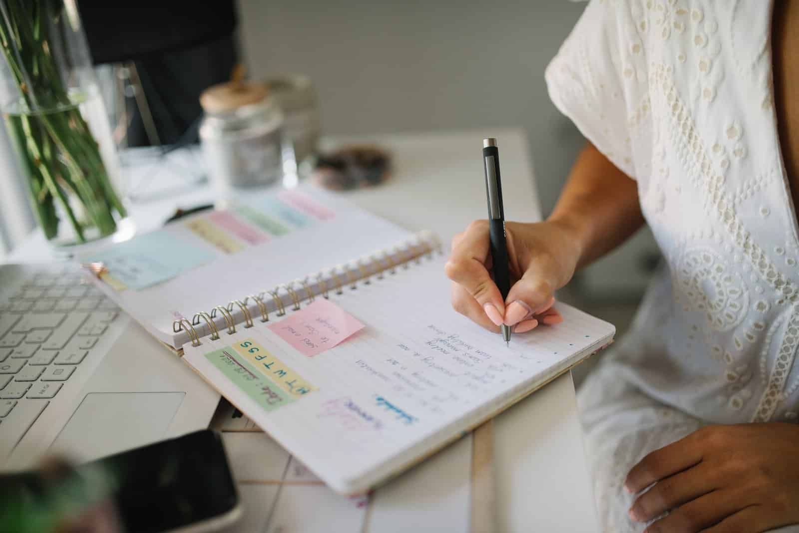Woman writing in a spiral planner with colorful sticky notes