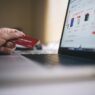 Hand holding a credit card next to a laptop
