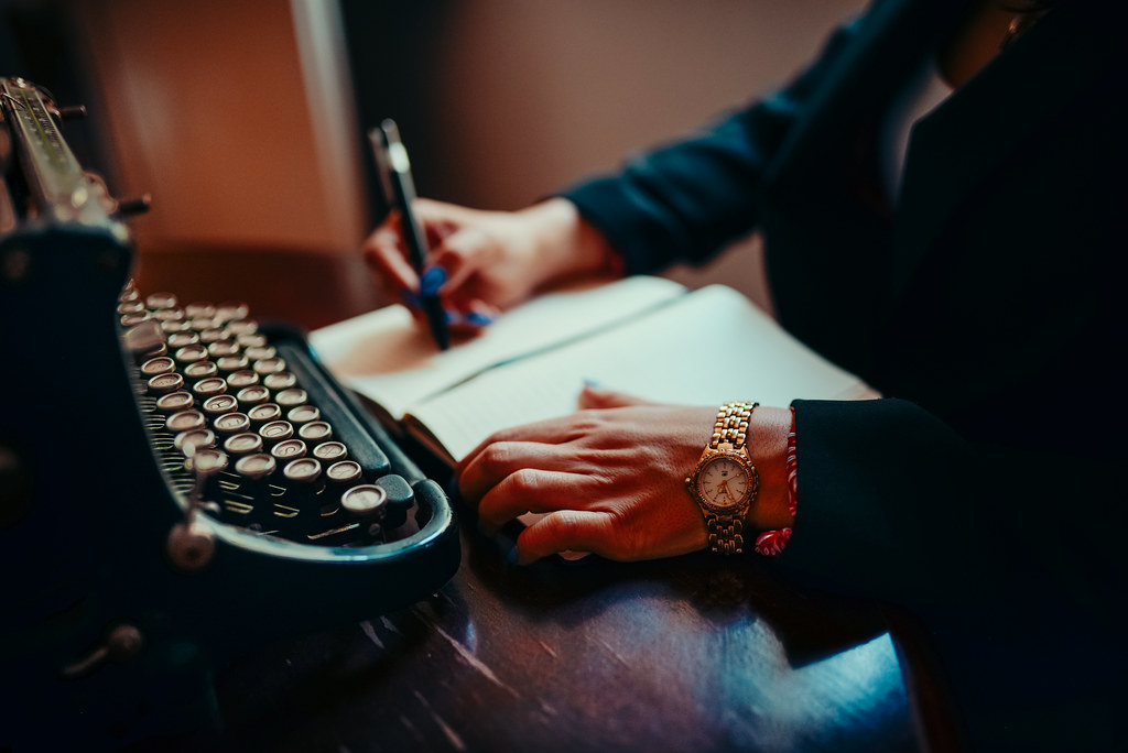 Person writing study notes in a notebook next to a vintage typewriter