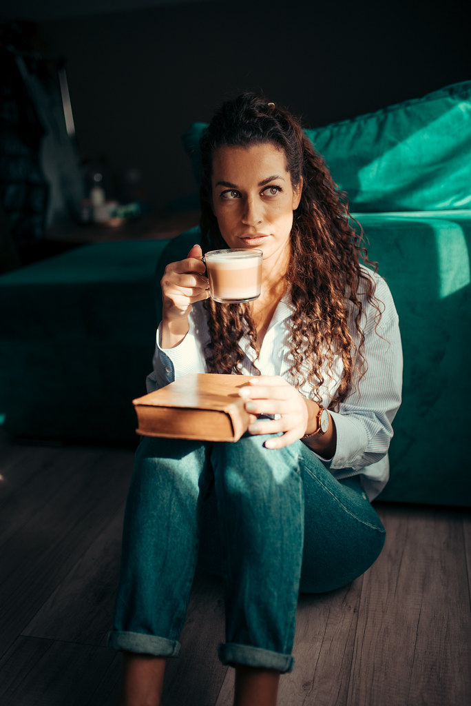 Person enjoying coffee while reading a book in a cozy living room