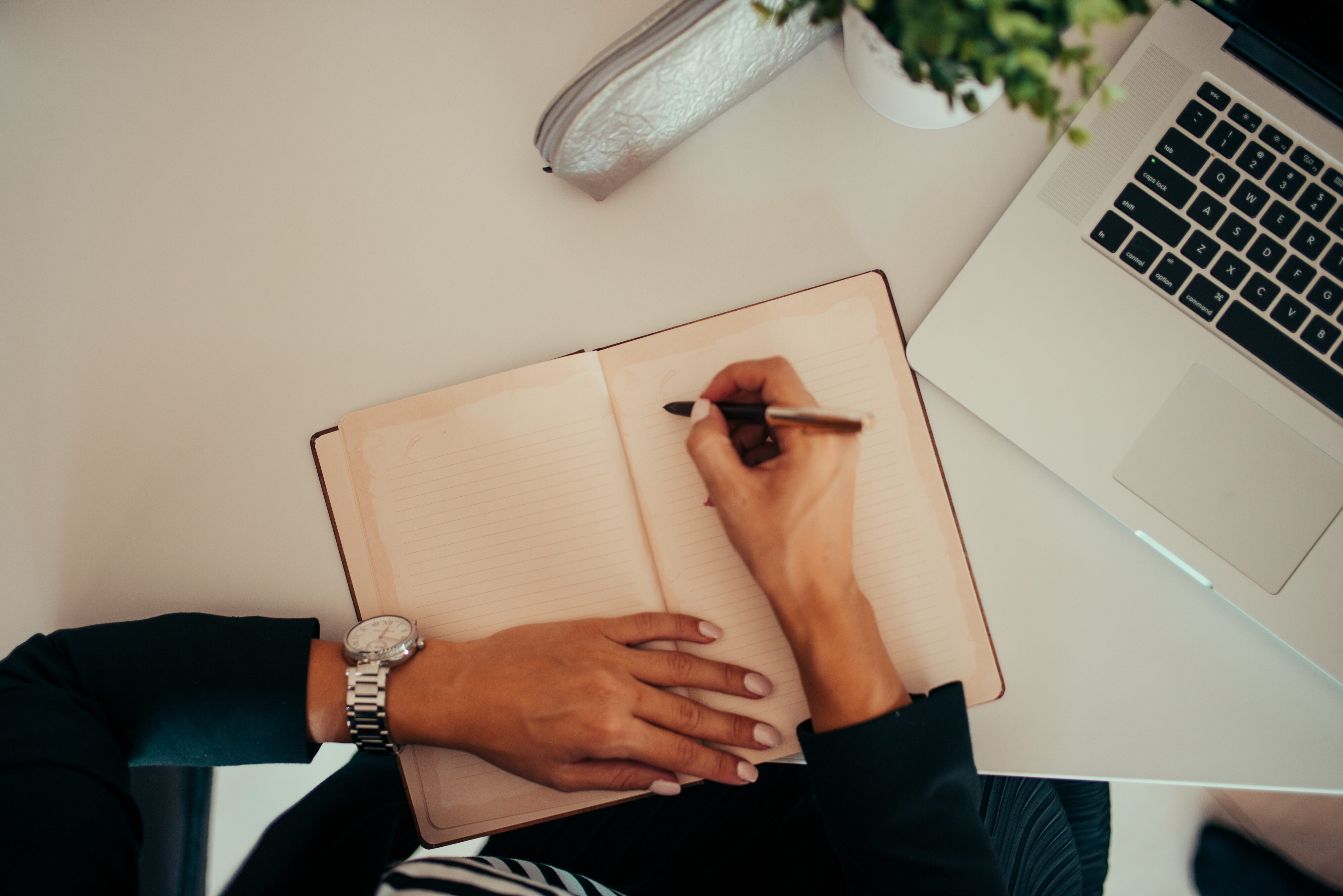 Person writing in notebook at a modern workspace with laptop