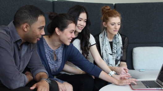 Four students gathered around a laptop learning together