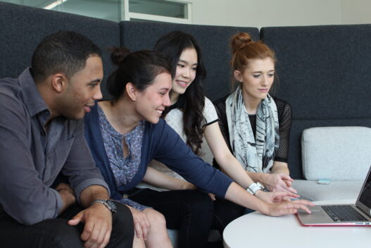 Four students gathered around a laptop learning together