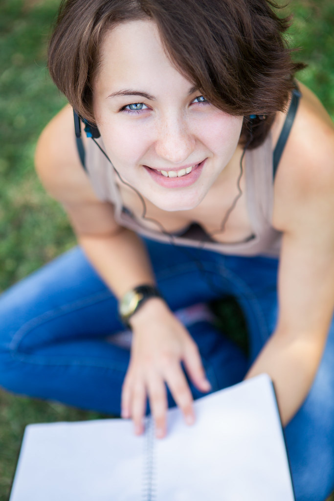 Young woman studying outdoors with earbuds and notebook