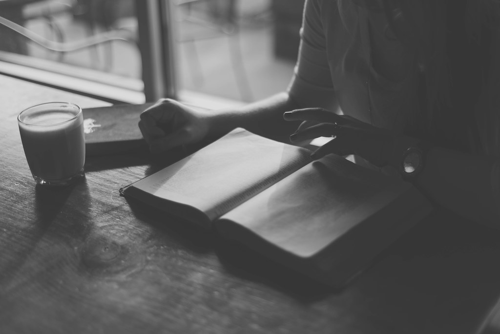 Person reading a book by a window in black and white