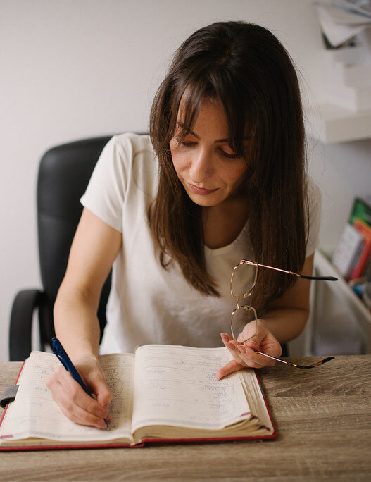A woman writing notes in a notebook at a wooden desk