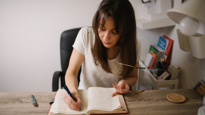 A woman writing notes in a notebook at a wooden desk