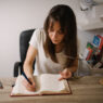 A woman writing notes in a notebook at a wooden desk