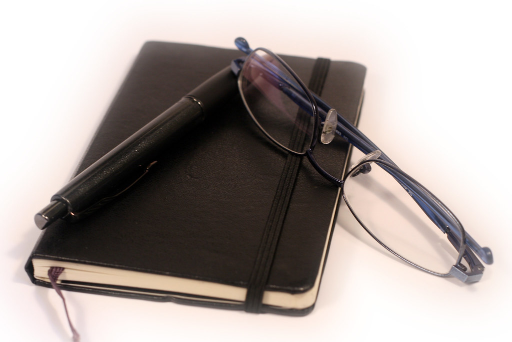 A pen, diary and glasses arranged on a desk