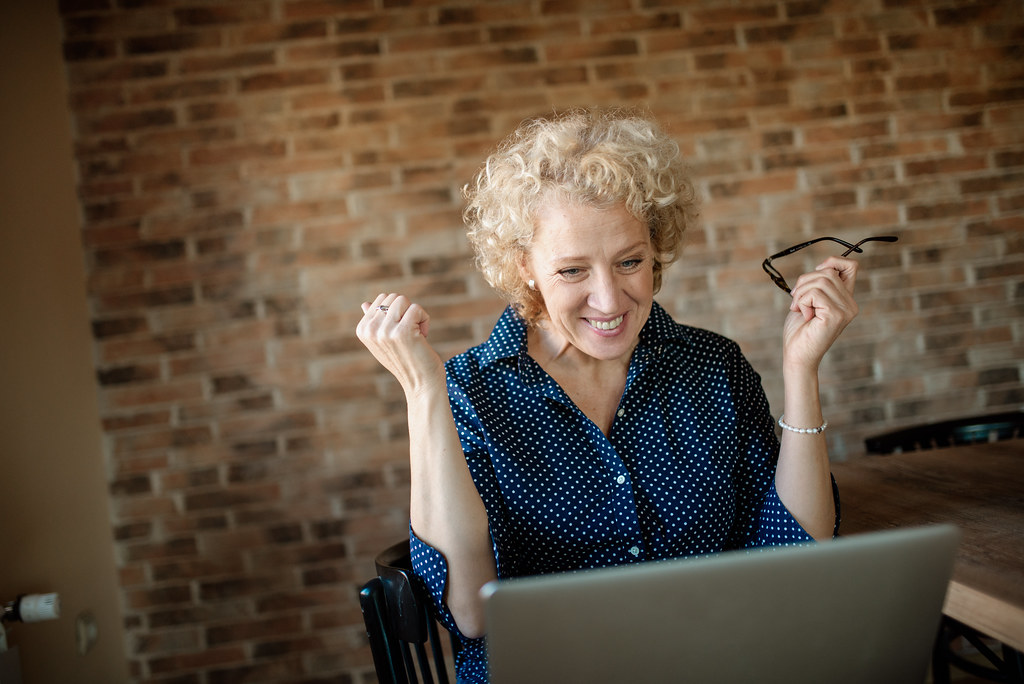 A cheerful older woman holding her glasses and smiling