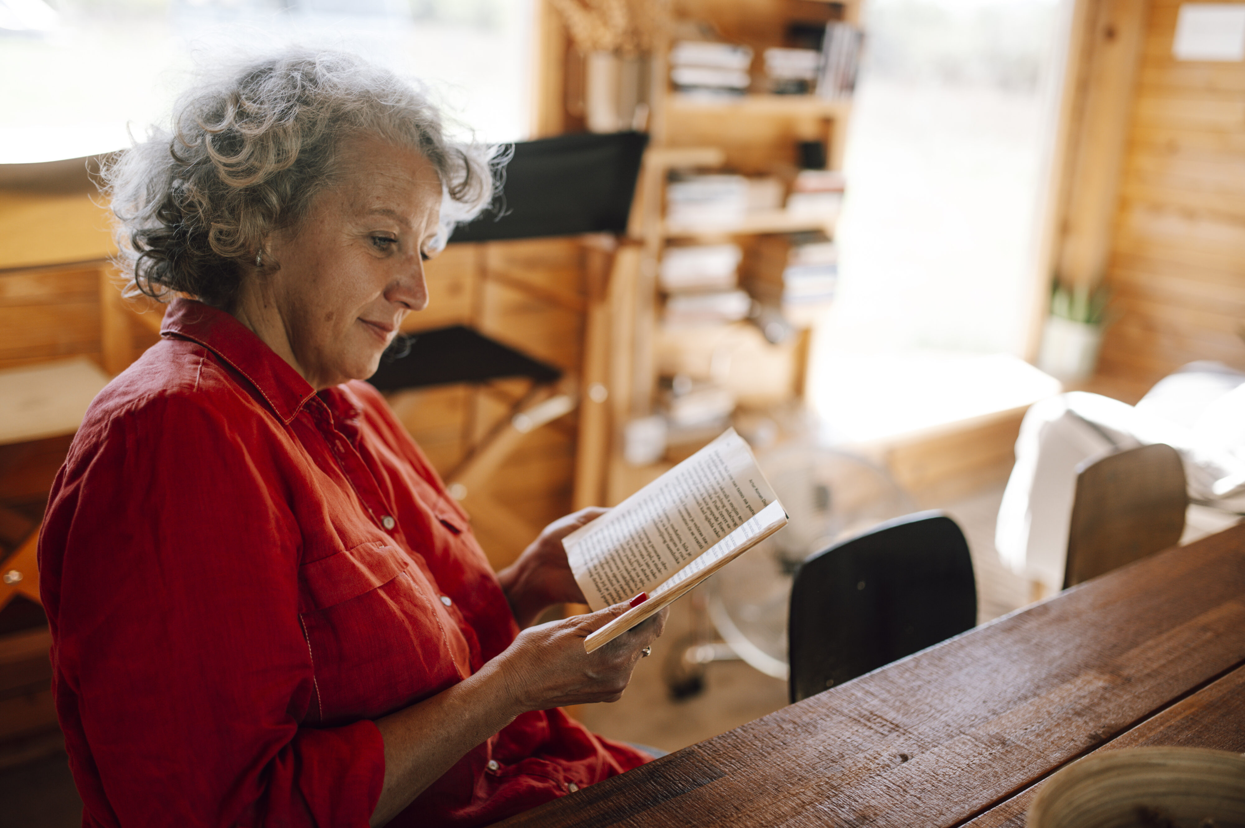 An older woman reading a book in a cozy wooden room