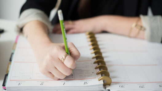 A hand writing in a planner with a pen