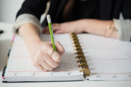 A hand writing in a planner with a pen