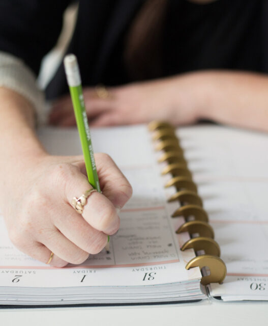 A hand writing in a planner with a pen