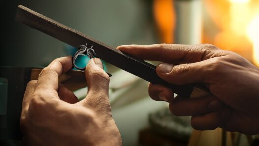 Hands filing a metal ring at a jeweler's workbench