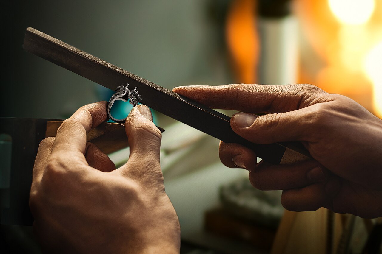 Hands filing a metal ring at a jeweler's workbench