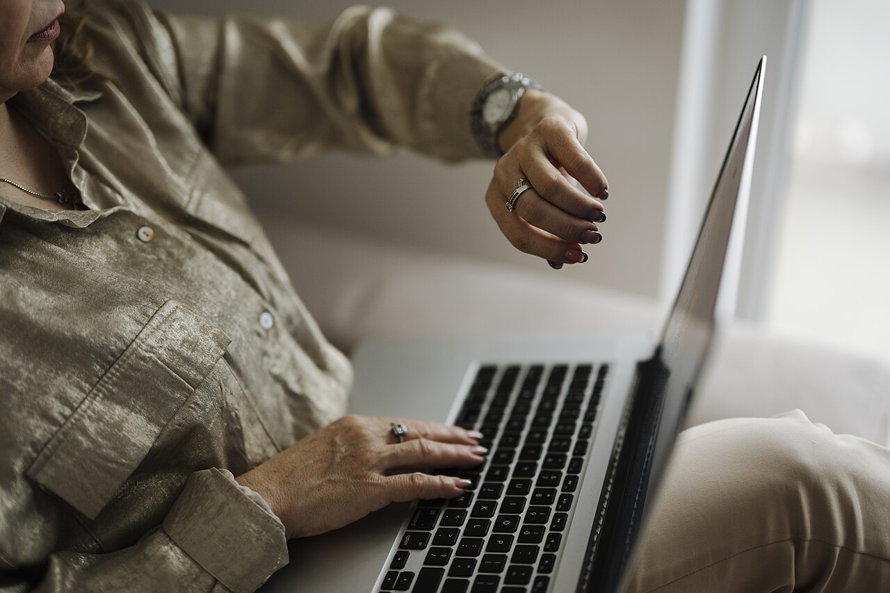 Woman typing on laptop at home, checking the time