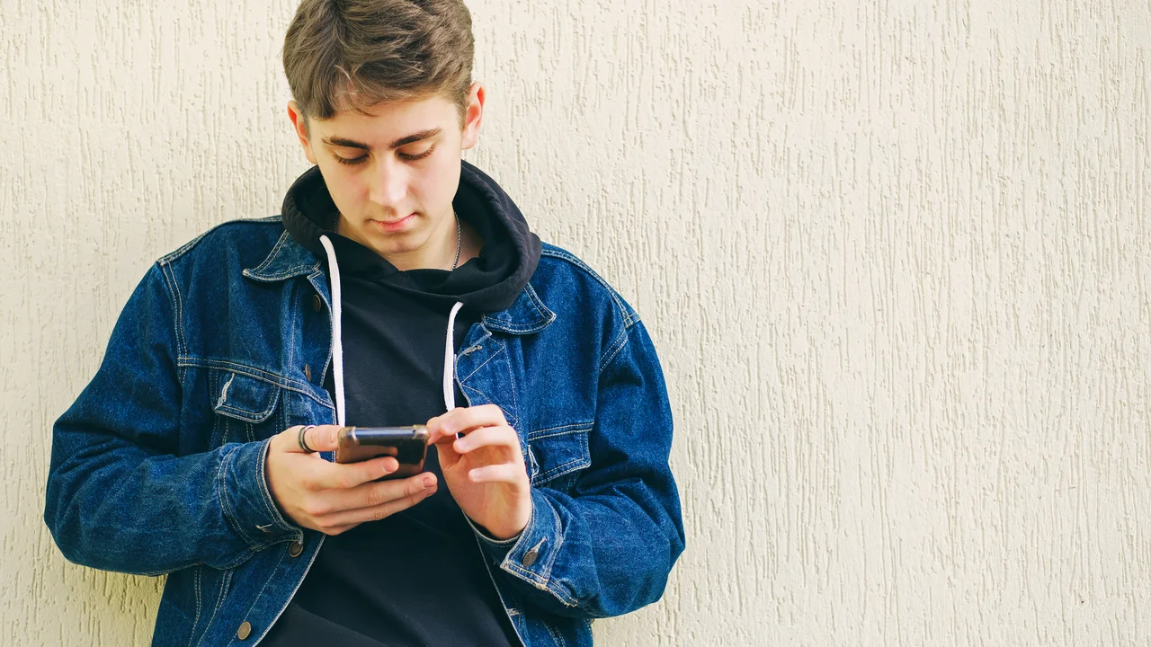 Teenager typing a text message on the phone - the young man uses the phone