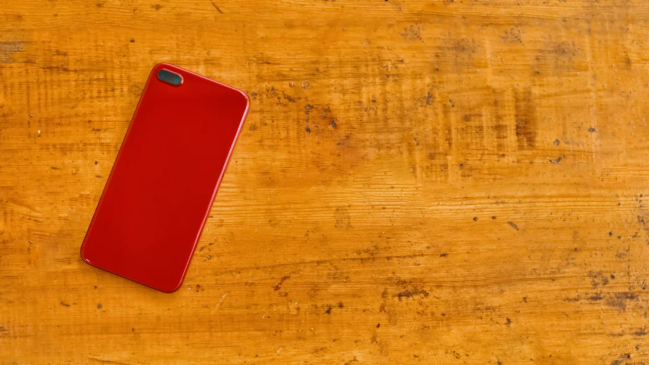 Red smart phone lies face down on wooden table. top view