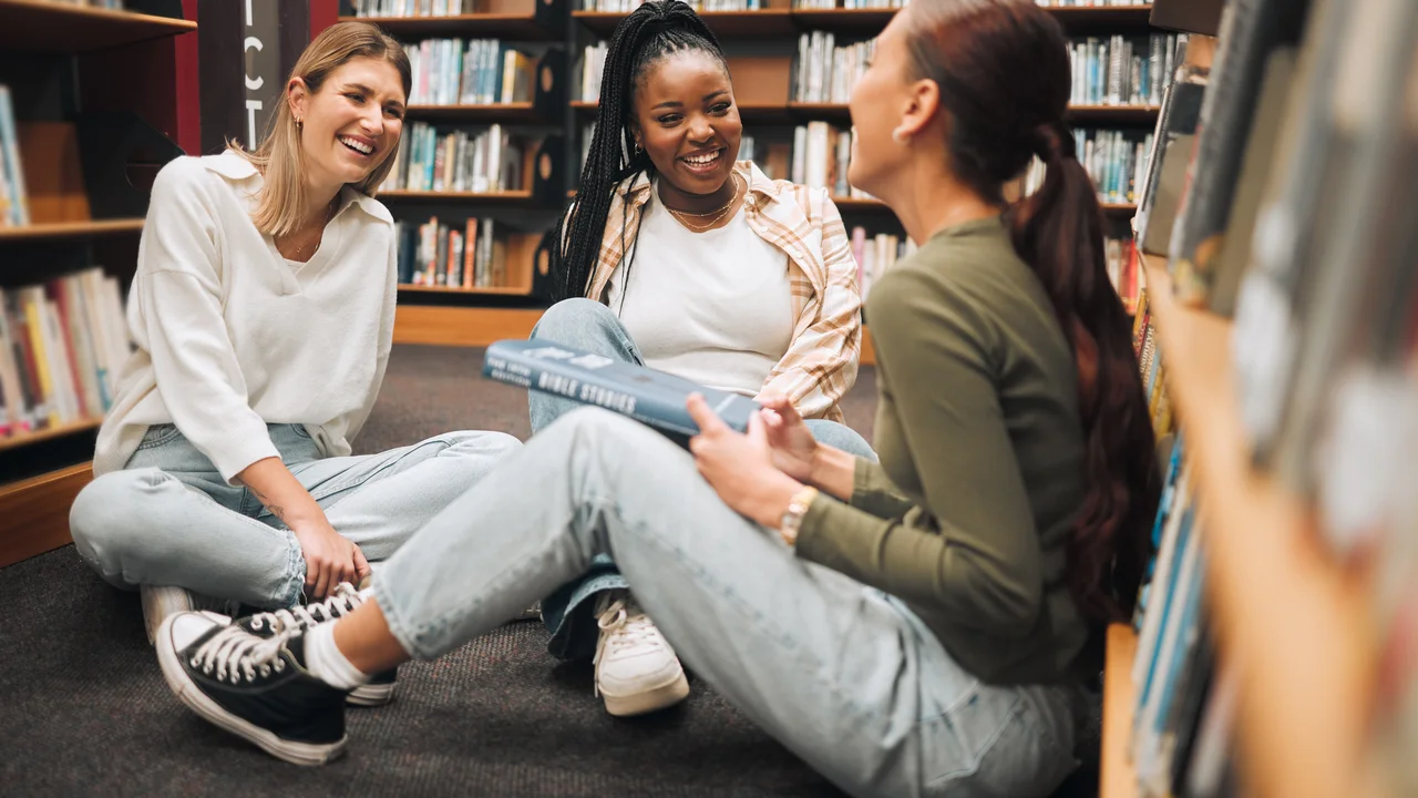 Education students or women friends on library floor for comic conversation learning or book study diversity happy or girl with smile for university support college research or school project
