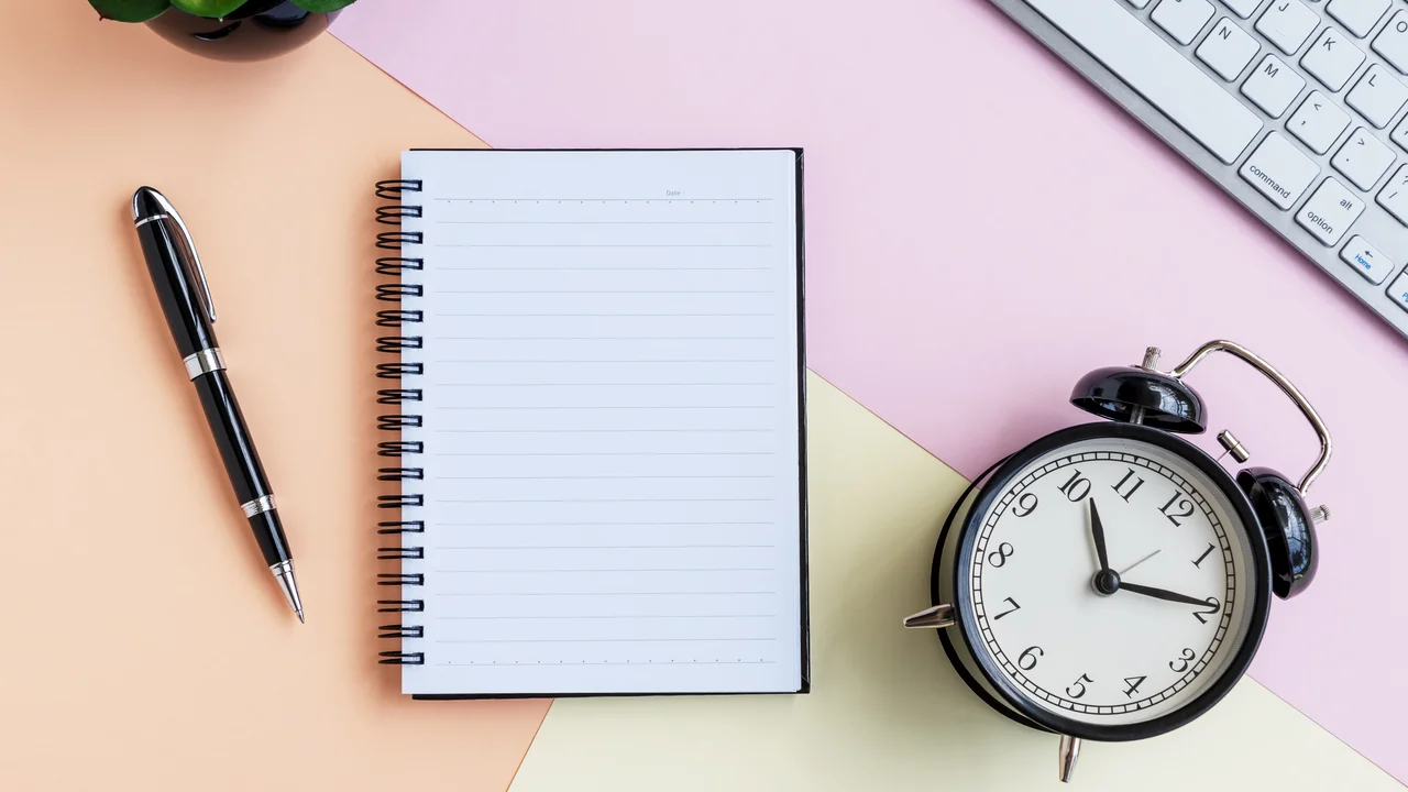 Alarm clock note pad computer keyboard green potted plant and pen on pastel colored background