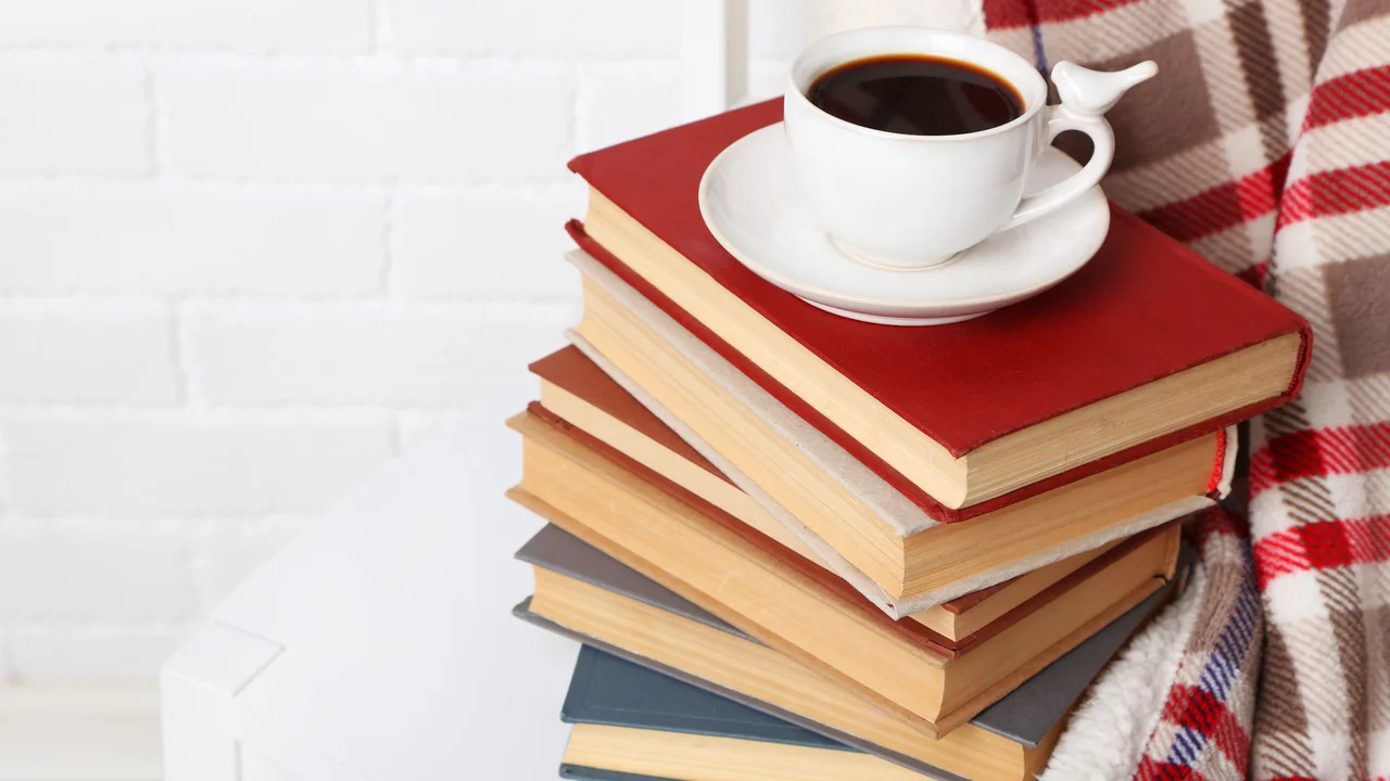 Pile of books with cup and plaid on the chair on brick wall background