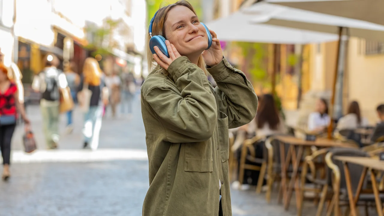 Rear view of young woman tourist with backpack listening music via headphones walking through street