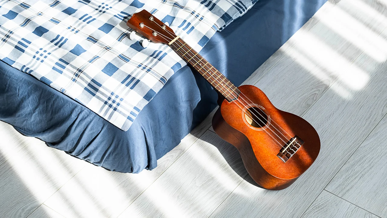 Ukulele guitar resting on bed hawaiian acoustic guitar in bedroom