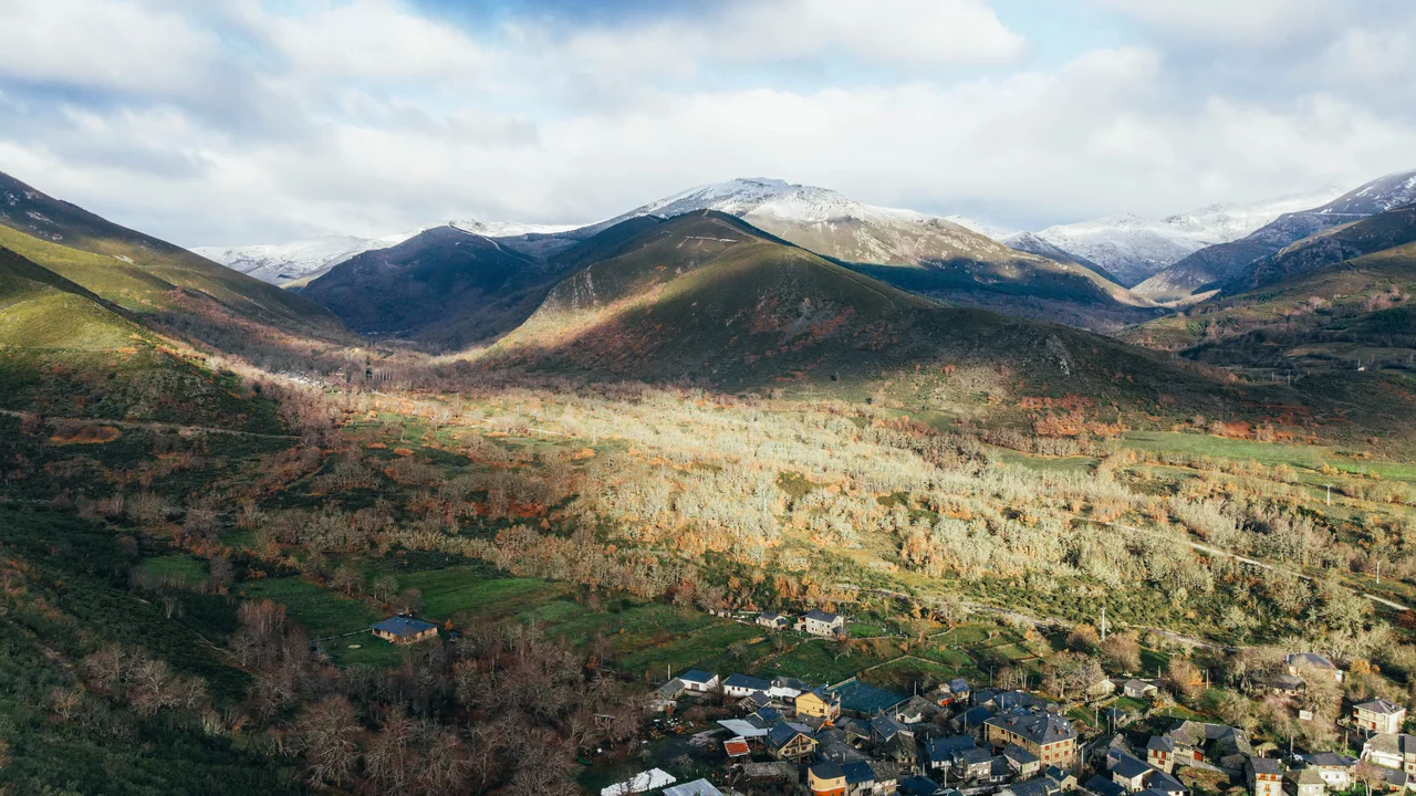 Drone view of a village surrounded by green and snowcapped peaks mountains